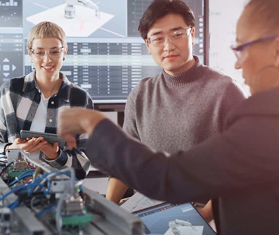 Two females and one male manufacturing workforce professionals use a robot during manufacturing fundamental training.