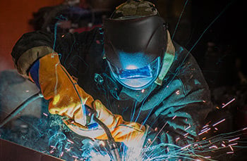 welding professional in protective clothing and head gear welds machining part